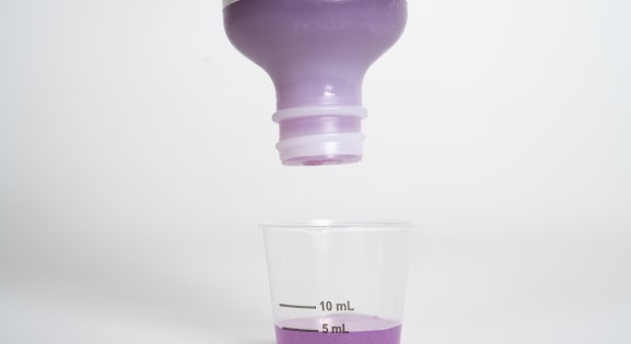 Purple liquid medicine being poured into dosing cup