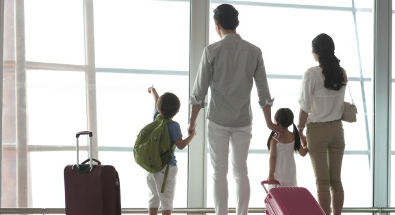 family with suitcases facing away looking out a window