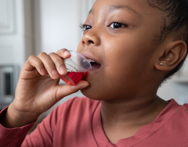 African American/Black girl in red shirt drinking liquid medicine