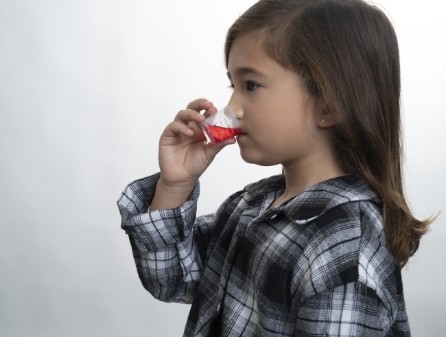 Racially ambiguous girl with dark hair in plaid shirt drinking medicine against white background